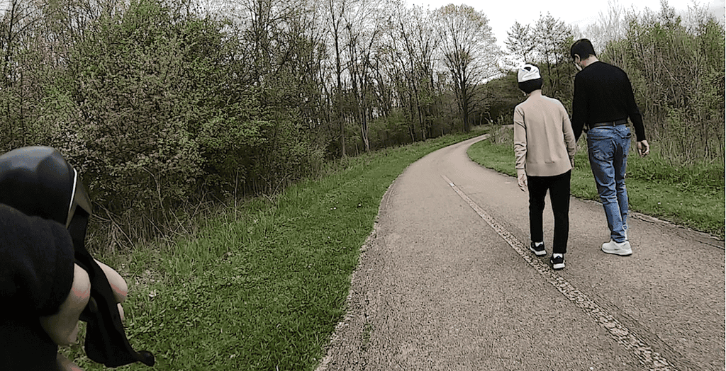 A couple in sweaters walks to the middle yellow line of a bike trail, from the vantage point of a cyclist.