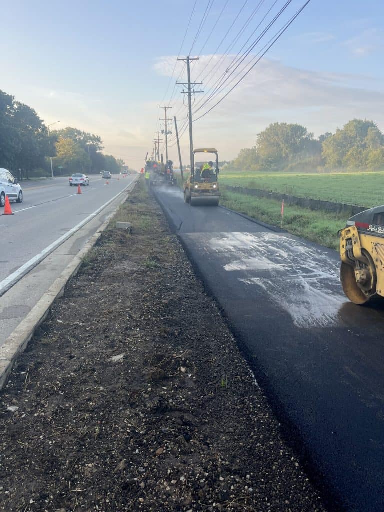 Asphalt path construction off a suburban road going by farmland and trees