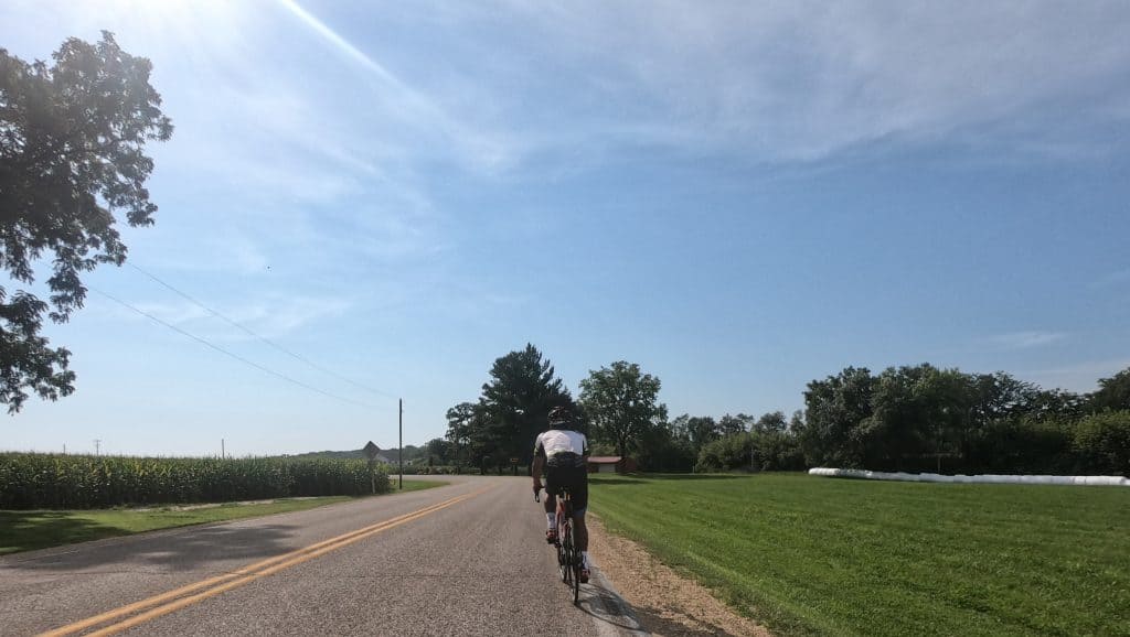 Cyclist riding on a rural road in suburban Chicago with clear blue sky.