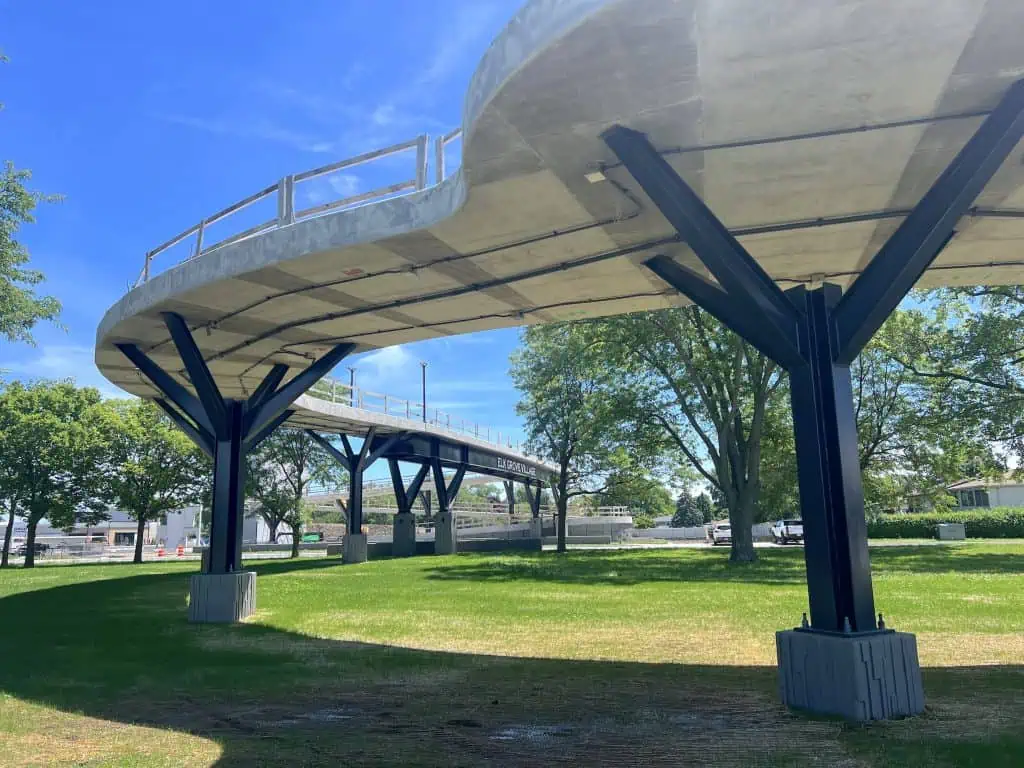 Modern elevated bike bridge with supporting columns and green park surroundings.