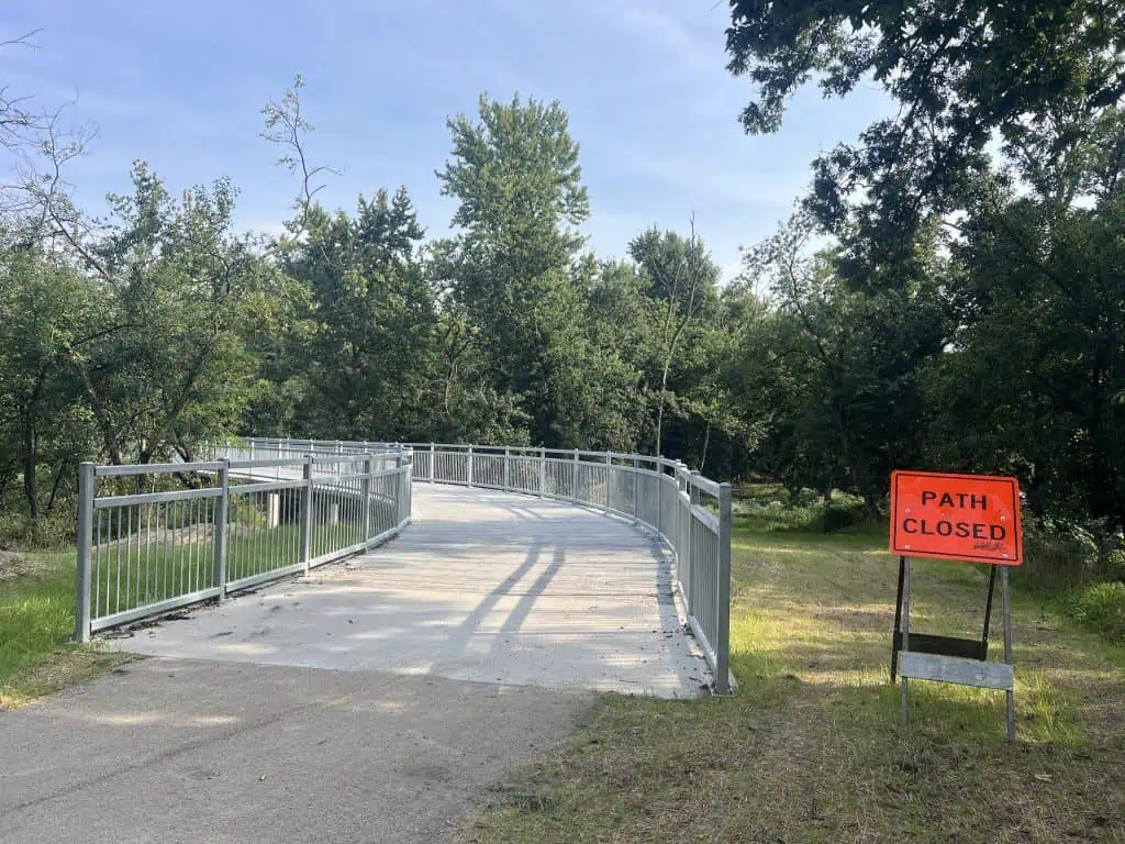 Pedestrian bridge with a orange 'Path Closed' sign to the right of it in a park setting.