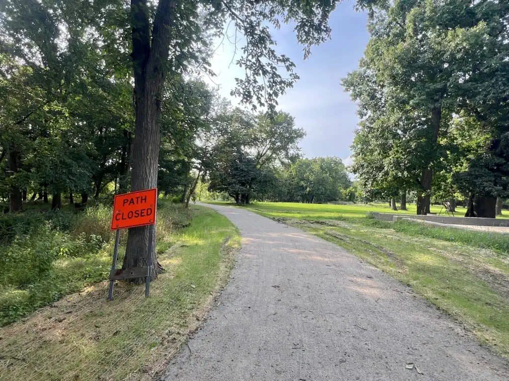 Path closed sign on a gravel trail in a park with trees and grass.